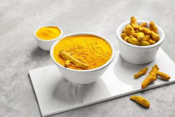 Bowls with turmeric powder and roots on grunge background