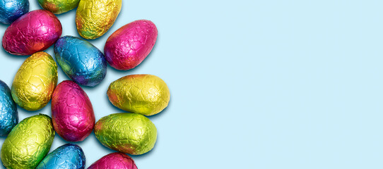 Side border of colorful wrapped chocolate Easter eggs on blue background. Top view. 