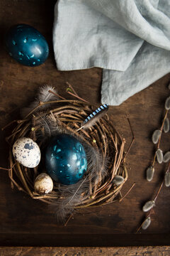 nest with easter eggs, feathers and pussy willow twigs on wooden background