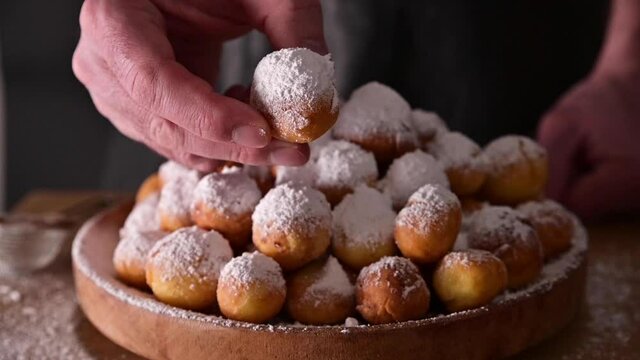 A man shows a sweet bun. Baked castagnole with powdered sugar. Traditional sweet pastries in hand. Street food, round biscuits with sugar for the carnival of Venice. carnival period in italy .