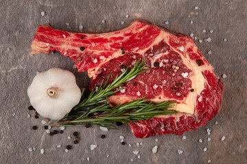 Raw meat with a bone on a gray background. Garlic, rosemary, salt.