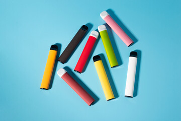 Layout of colorful disposable electronic cigarettes with shadows on a blue background. The concept of modern smoking, vaping and nicotine. Top view