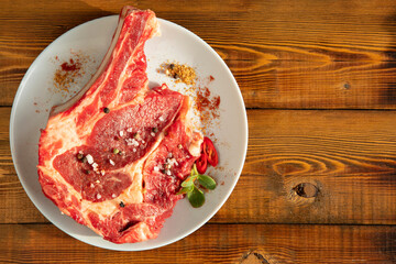 Raw meat with a bone on a white plate. Wooden table. Top view. Copy space.