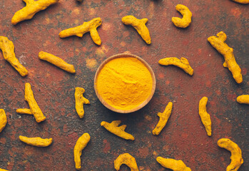 Bowl with turmeric powder and roots on grunge background