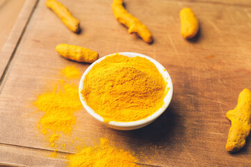 Bowl with turmeric powder and roots on board, closeup