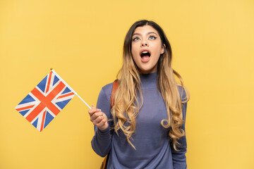 Young Russian girl holding an United Kingdom flag isolated on yellow background looking up and with surprised expression