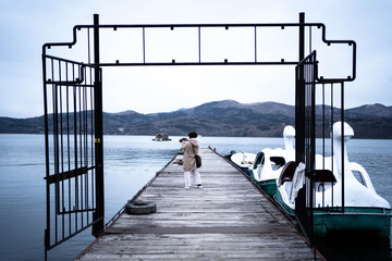湖の桟橋で写真撮影を楽しむ女性とその桟橋の横にある白鳥のボートたち