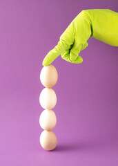 Four eggs arranged vertically are held by a hand in a green glove. Easter decoration on  purple background.