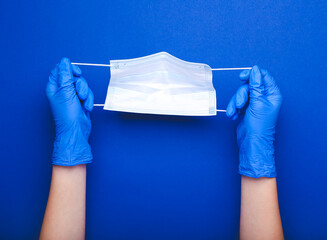 Female hands in protective gloves with medical mask on color background