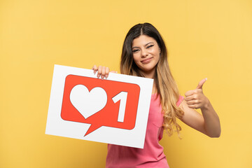 Young Russian girl isolated on yellow background holding a placard with Like icon with thumb up