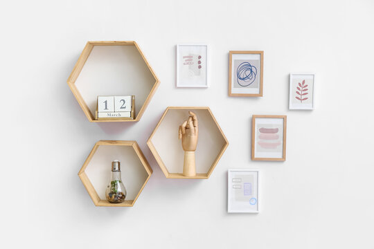 Stylish pictures and shelves with decor hanging on light wall
