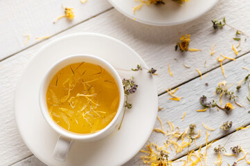two cups of aromatic flower tea, soothing, medicinal on white wooden background