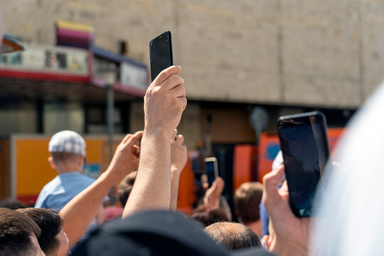 phone in hand holds over the crowd to take photos