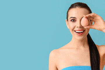 Beautiful young woman with makeup sponge on color background