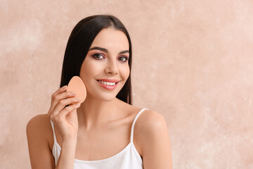 Beautiful young woman with makeup sponge on color background