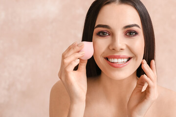 Beautiful young woman with makeup sponge on color background