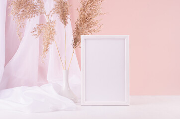 Calm home decor with blank photo frame for text, silk curtain, fluffy reeds bouquet on white wood table, pink wall. Template for display and portfolio.