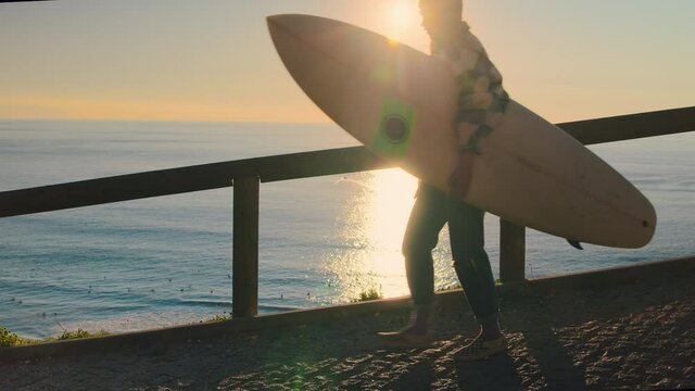 Slow motion of woman walk down to beach with surfboard. Concept surf school lesson or surfing camp in Portugal. Cinematic surf lifestyle sunrise or sunset shot