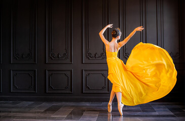 elegant ballerina in pointe shoes dances with flowing yellow fabric on a dark gray background
