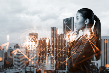Attractive young Asian HR director at international company is thinking about recruitment of highly qualified specialists. Women in business concept. Social media hologram icons over Kuala Lumpur.