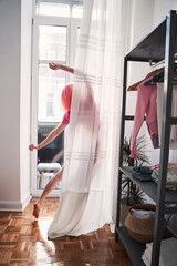 Woman standing and stretching at window in bedroom with relaxation