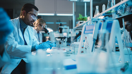 Team of Medical Research Scientists Conduct Experiments with Help of Microscope, Test Tubes, Micropipette and Tablet Computer. Modern Biological Applied Science Laboratory with Diverse Colleagues.