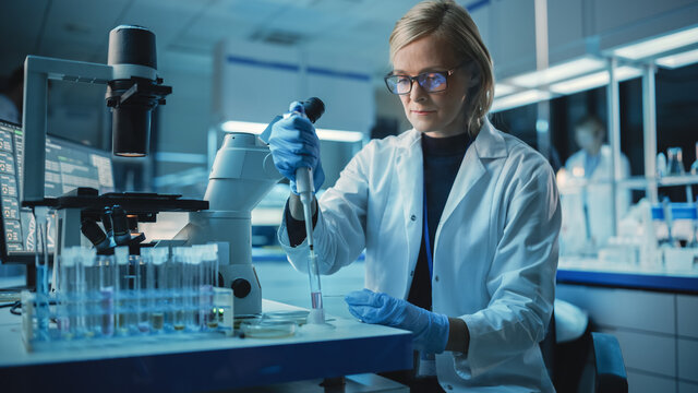 Female Research Scientist is Wearing Glasses and Using Micropipette to Extract a Sample on a Microscope Slide to Make Analysis of it. Scientists Workingin Modern Laboratory with Help of Technologies.