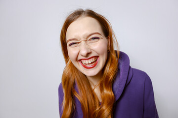 Laughing redhead girl in purple hoodie. Light background