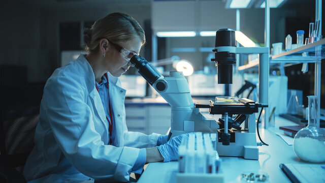 Medical Research Scientist Looks at Biological Samples Under Digital Microscope in Applied Science Laboratory. Beautiful Caucasian Lab Engineer in White Coat Working on Vaccine and Medicine.