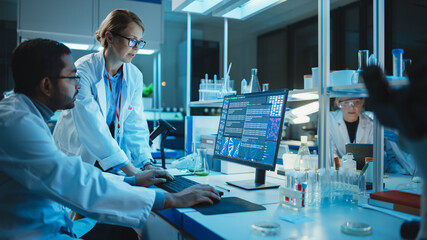 Female Research Scientist with Bioengineer Working on a Personal Computer with Screen Showing Gene Analysis Software User Interface. Scientists Developing Vaccine, Drugs and Antibiotics in Laboratory