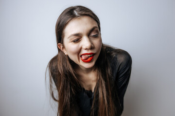 The woman shows her tongue, teases. Close-up portrait on a light gray background.