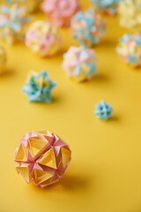 Set of multicolor handmade modular origami balls or Kusudama Isolated on yellow background. Visual art, geometry, art of paper folding, paper crafts. Close up, selective focus, copy space.