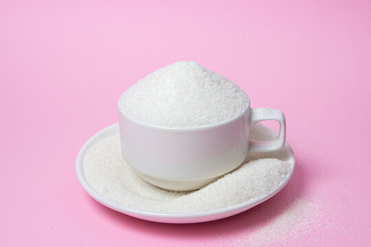 Excessive sugar intake. Sugar on a pink background. An overflowing cup of sugar.