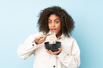 Young African American woman isolated on blue background holding a bowl of noodles with chopsticks...
