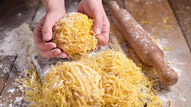 Tagliatelle pasta in hand. Traditional Italian named Angel Hair (capellini d'angels). Woman cooking Italian egg pasta, homemade and fresh in flour on a cutting table. vertical video for social media