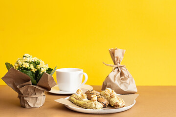 Spring still life, bouquet of yellow flowers, craft paper bag with a gift, eclairs and a cup of tea. Mothers day concept. Composition with copy space