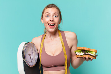 young pretty sport woman surprised expression and holding a scale and a sandwich