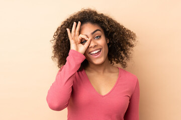 Young African American woman isolated on beige background showing ok sign with fingers