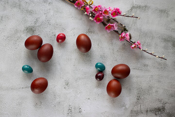 Beautiful branches with bright pink flowers and decorative Easter eggs on a cement background. Easter concept. Top view.