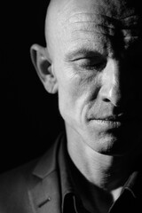 Black and white portrait of a brutal bald middle man with closed eyes. Charismatic pensive man on a black background. Close-up portrait of half of the face.
