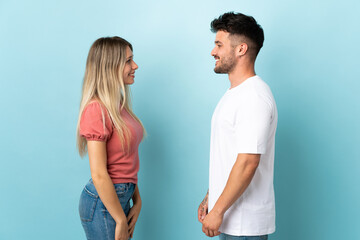 Young caucasian couple isolated on blue background looking at each other