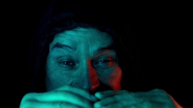 middle-aged man, stalker in hood looks through black binoculars in dark, peeps, illegally tracks down personal secrets of neighbors, concept of industrial espionage, surveillance