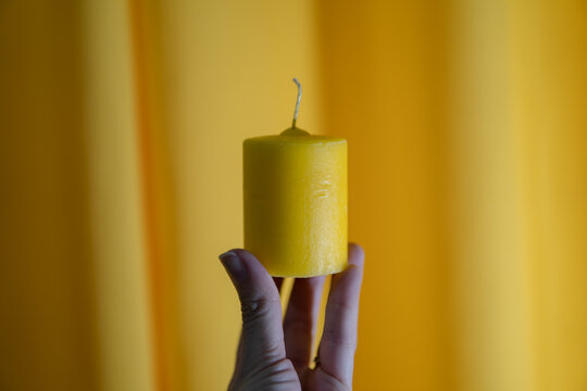 white hand holding yellow candle in front of yellow background