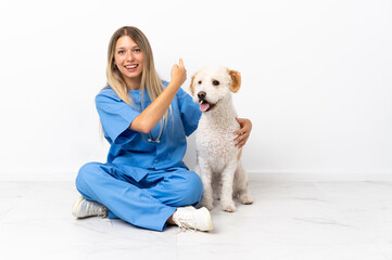 Young veterinarian woman with dog sitting on the floor pointing back