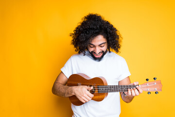 Obraz premium A cute young egyptian man with a beard holds a small guitar in his hands and plays it