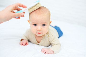 mom combs the baby with a special hair brush on a white background. Child hygiene.