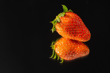 A sweet soft red fruit with a seed-studded surface were cut in half on the mirror with a black background..
