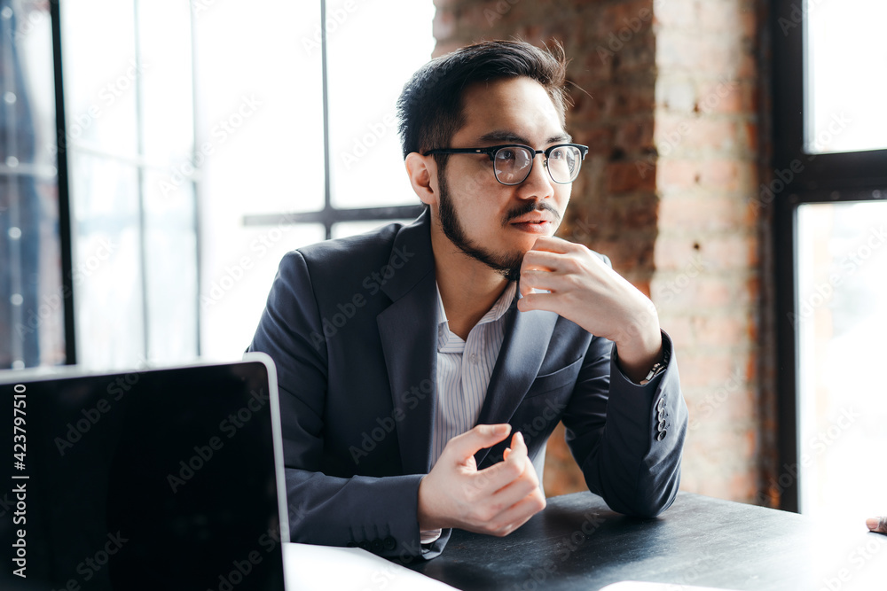 Canvas Prints Young korean student wearing glasses sits at a table and listens attentively to others in a meeting