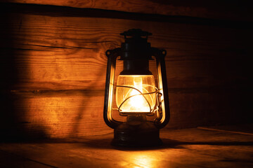 Oil lantern burning with glow soft light on aged wooden surface. Kerosene lamp in dark room.