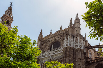 Obraz premium Fragment facade of Sevilla Cathedral, La Giralda bell tower with statue El Giraldillo on his top and Oranges. Cathedral of Saint Mary of the See, Seville; Andalusia, Spain, Europe.